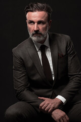 Obraz premium Portrait of a stylish elegant senior businessman with a beard and casual business clothes in photo studio isolated on dark background gesturing with hands