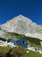 Fototapeta na wymiar Peak of mountain Dolkova Spica in Triglav national park and Julian alps in Slovenia with a mountain shelter made of metal on alpine landscape with meadows and creeping pine in front