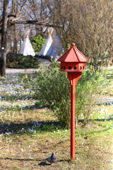 Cute red birdhouse in the beautiful park. Early spring day. Selective focus.