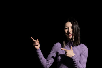 brunette woman on black background pointing to her right