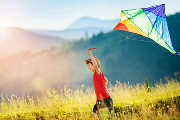 Little happy boy running in the mountains with kite. Beautiful mountain landscape at sunset. Toys for summer vacation.