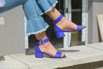 Women's legs in blue denim jeans and sandals in the city street. Trendy elegant casual outfit....