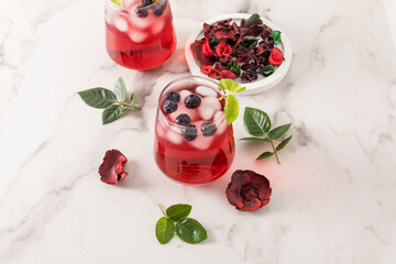 tonic vitamin drink from rose petals hibiscus with blueberries, mint leaves, ice cubes in glasses on a marble table. iced tea.
