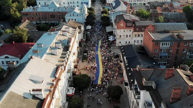 Drone shot of many people holding a huge flag of Ukraine in Sumy. A huge Ukrainian ensign in the city center, drone view. Independence Day of Ukraine in the city of Sumy. United people of Ukraine