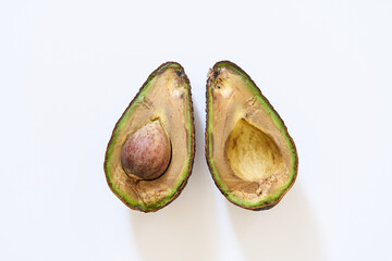 A rotten avocado on a white background. The overripe avocado is cut in half. The core is in the...