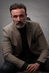 Fototapeta premium Portrait of a stylish elegant senior businessman with a beard and casual business clothes in photo studio isolated on dark background gesturing with hands
