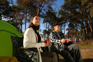 Fototapeta na wymiar Couple resting in camping chairs and enjoying hot drink outdoors