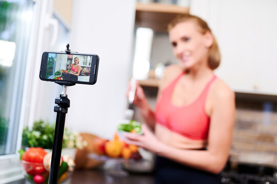 Selective focus. Healthy food blogger female cooking fresh vegan salad of fruits, filming tutorial on camera for video channel. Female influencer shows no junk food thumb up gesture