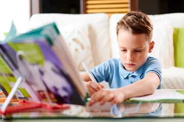 Caucasian Schoolboy at his desk doing his maths homework. Home schooling or Distance learning