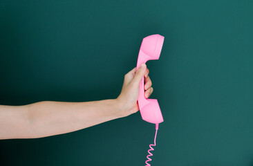Woman hand holding vintage telephone receiver isolated on green background
