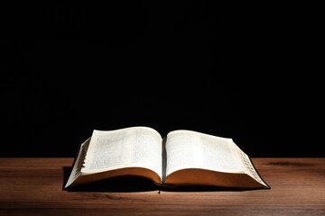 Open Bible on wooden table against black background. Christian religious book