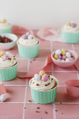 Easter egg cupcakes in mint green cases set against a pale pink background. Pastel spring colour theme. Chocolate easter egg celebration food.