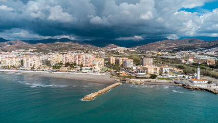 Drone perspective of costal city of Torrox situated in Malaga, Costa del Sol, Spain. Touristic travel destination. View of the promenade and beach area. The lighthouse of Torrox and the river.