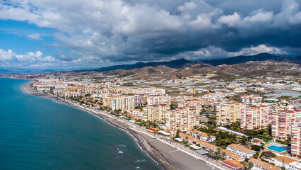 Fototapeta na wymiar Drone perspective of costal city of Torrox situated in Malaga, Costa del Sol, Spain. Touristic travel destination. View of the promenade and beach area. The lighthouse of Torrox and the river.