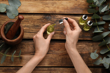 Woman holding bottle of eucalyptus essential oil at wooden table, top view