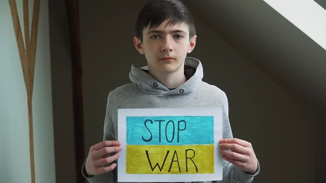 Boy holding self made picture with text Stop war on background of Ukrainian flag in refugee camps. Crisis, peace, stop aggression in whole world