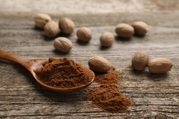 Spoon with nutmeg powder and seeds on wooden table, space for text