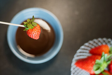 a strawberry about to be dipped in melted chocolate
