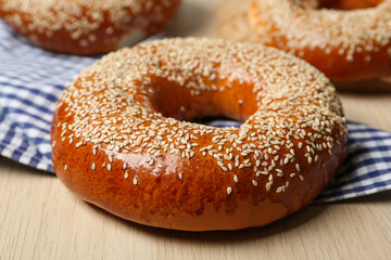 Delicious fresh bagel with sesame seeds on light wooden table, closeup