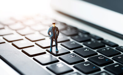 Miniature businessman standing on laptop keyboard