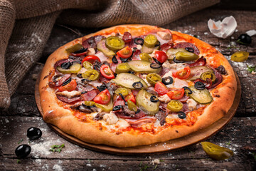 pizza with salami barbecue sausages ham tomatoes bell peppers on a wooden board sprinkled with flour