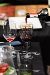 Pouring red wine into the glass against served table background.