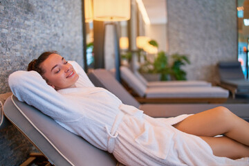 Carefree satisfied serene female with hands behind head lying on chaise longue chilling and relaxing alone in spa center. Mind health and getaway
