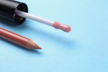 Lip pencil and brush of liquid lipstick on light blue background, closeup view with space for text. Cosmetic product