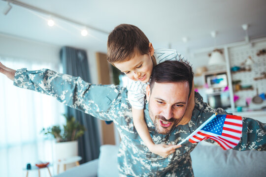 Happy military man with his son at home. An emotional military father, dressed in camouflage, holds his young son in arms in greeting after returning home from a tour of duty overseas.