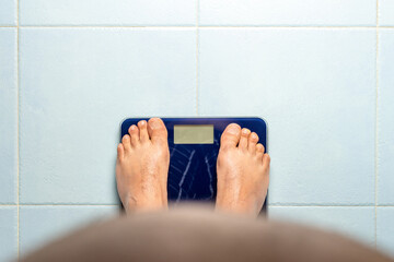 Man looks down at his belly while standing on a weight scale. Weight loss concept. High quality...