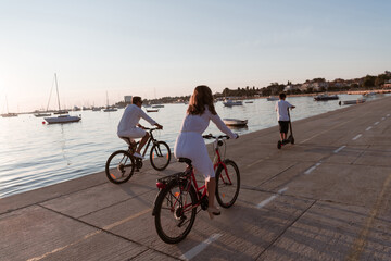 Fototapeta premium Happy family enjoying a beautiful morning by the sea together, parents riding a bike and their son riding an electric scooter. Selective focus 