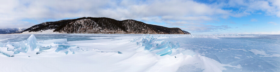 Panoramic view of coast of frozen Baikal Lake near Bolshoe Goloustnoye village. Beautiful winter landscape with snowy surface of blue ice with ice hummocks on cold January day. Natural background
