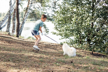 Boy playing with domestic puppy dog in park in outdoors. White Pomeranian puppy Child walking and training dog on leash in forest in summer