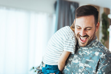 Young soldier just arrived home and he is so happy to see his son. Happy male soldier dad reunited with son after US army. Playful military man having fun with his small son at home.