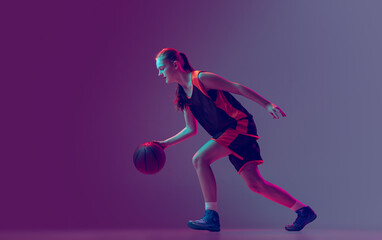 Fototapeta na wymiar Portrait of young girl, teen, basketball player in motion, training isolated over gradient pink purple background in neon. Side view