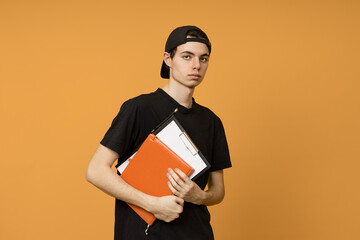 A young guy student in a black cap with notebooks in his hands on a yellow background