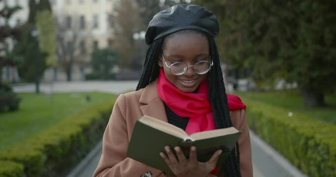 Black female student in a coat reads a book in the middle of the alley