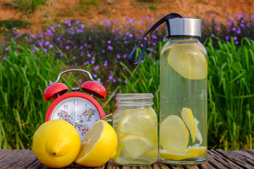 Freshness concept. Lemonade with alarm clock and lemon slices in a jar on a rustic  wooden background. Close up.