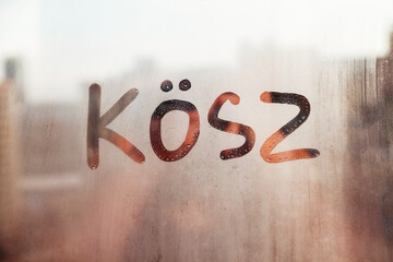Hungarian word Kosz thanks in english are painted on wet orange sunrise glass of window - obrazy, fototapety, plakaty