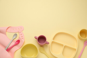 Flat lay composition with baby feeding accessories and bib on yellow background, space for text