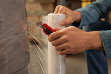 Worker wrapping boxes in stretch film at warehouse, closeup