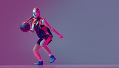 Fototapeta na wymiar Portrait of young girl, basketball player in motion, training isolated over gradient pink purple background in neon. Dribbling