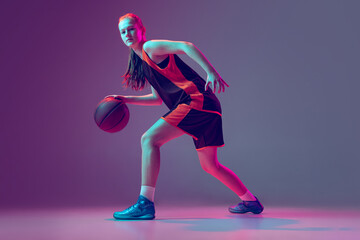 Fototapeta na wymiar Portrait of young girl, teen, basketball player in motion, training isolated over gradient pink purple background in neon