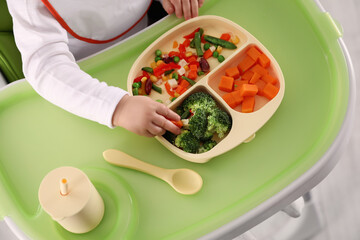 Little baby eating healthy food in high chair, closeup. Above view