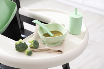High chair with food in baby tableware on tray indoors, closeup