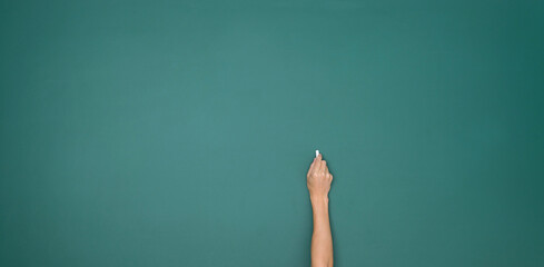 Hand holding white chalk and writing on green board