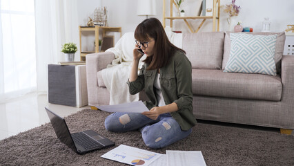 business school student under quarantine is asking about report via mobile phone while sitting on floor in living room.