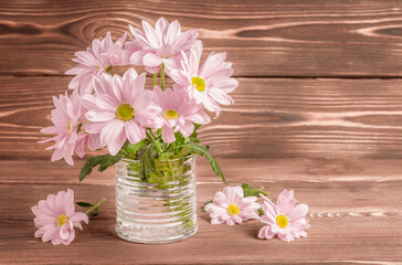 Pink chrysanthemums in a glass on a wooden table. Copy space