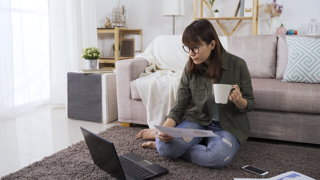 full length asian japanese woman accountant enjoy drinking morning coffee and preparing financial statement with document and personal computer during lockdown.