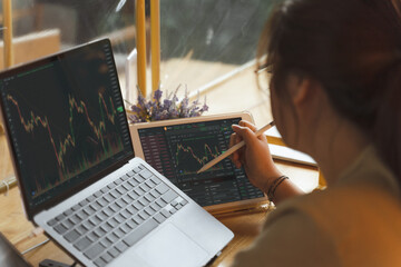 Asian Businesswoman, female trader, investor using laptop, tablet for stock market, Bitcoin cryptocurrency trading, strategy planning on money investing on online trading platform. Trading concept.